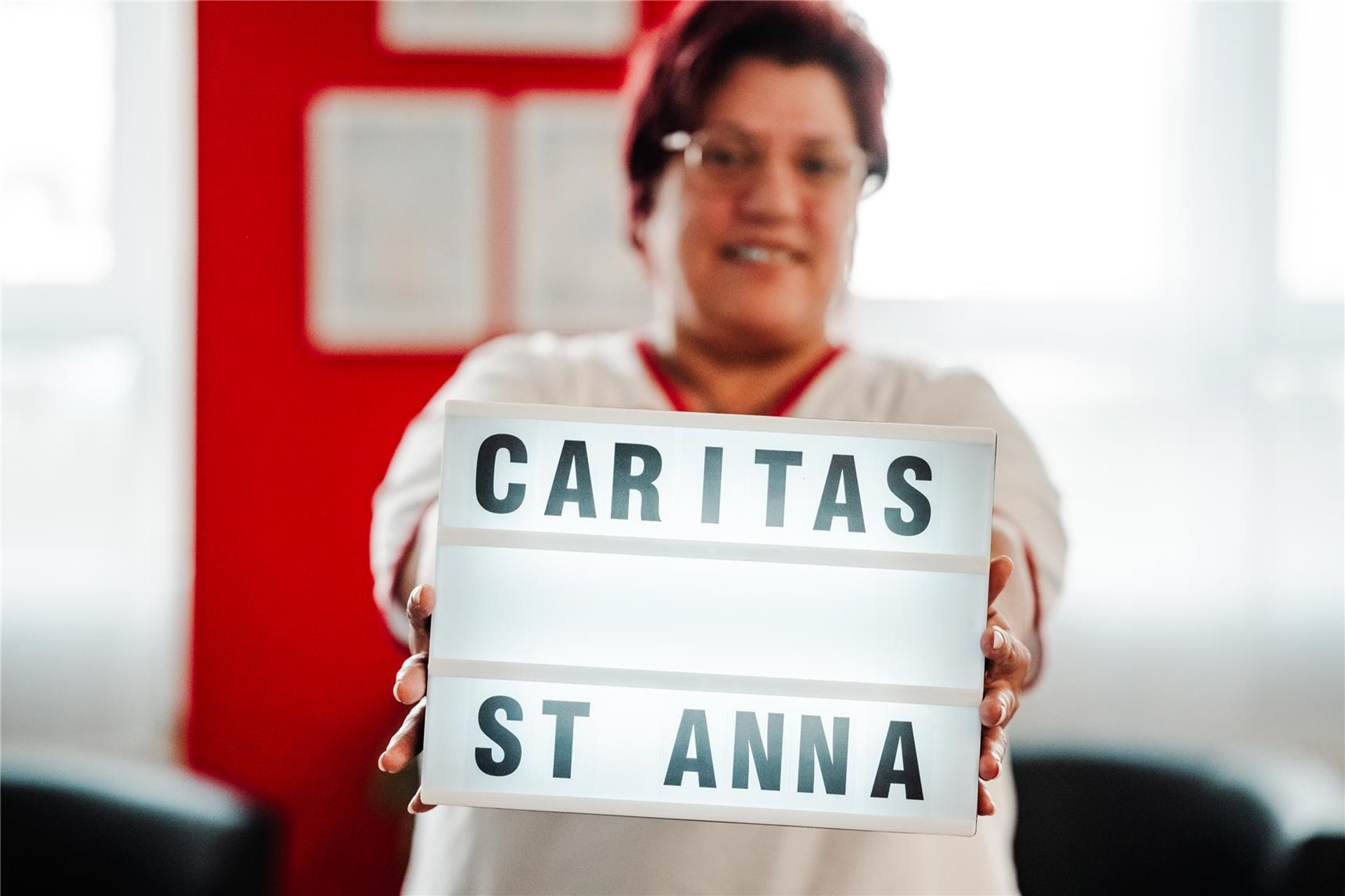 Eine Frau hält ein Display hoch, auf dem Caritas St. Anna steht.